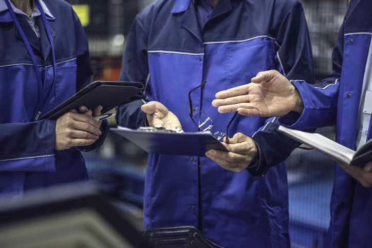 Mid section of factory engineers using digital tablet while discussing in appliance manufacturing factory.